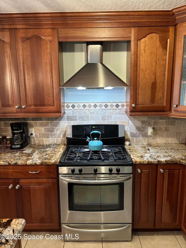 kitchen featuring light tile patterned floors, light stone countertops, decorative backsplash, gas range, and wall chimney exhaust hood