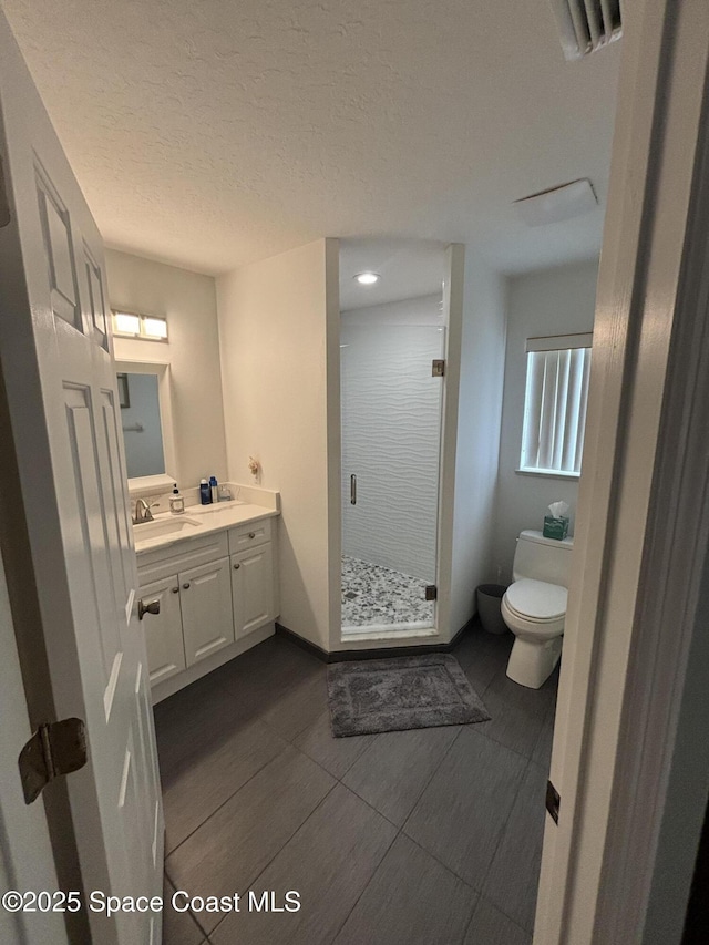 bathroom with a shower with door, vanity, a textured ceiling, and toilet