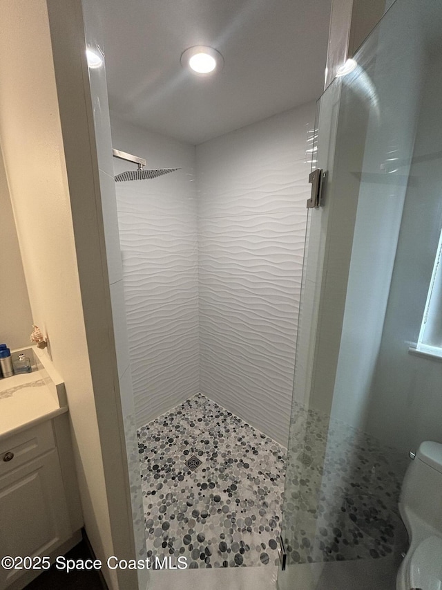 bathroom featuring vanity, a tile shower, and toilet