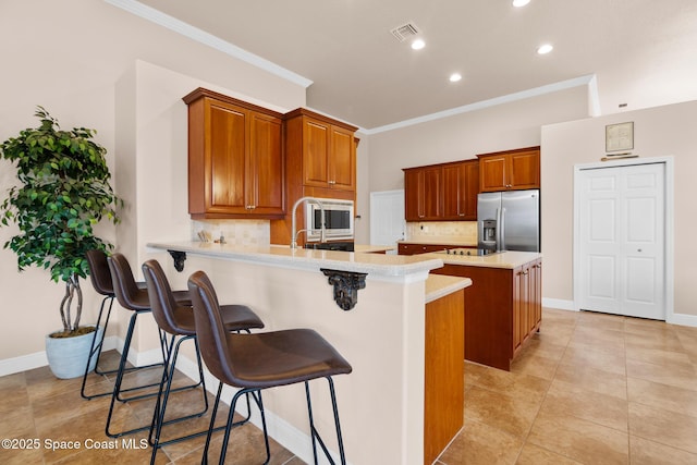 kitchen featuring crown molding, a breakfast bar area, appliances with stainless steel finishes, an island with sink, and decorative backsplash