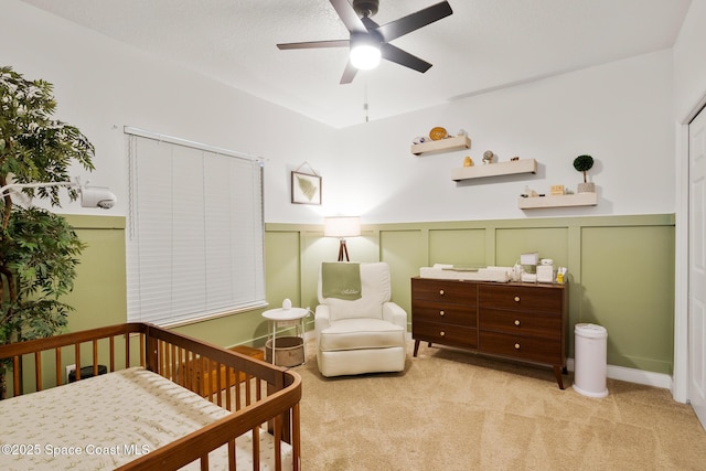 bedroom featuring ceiling fan, light carpet, and a crib