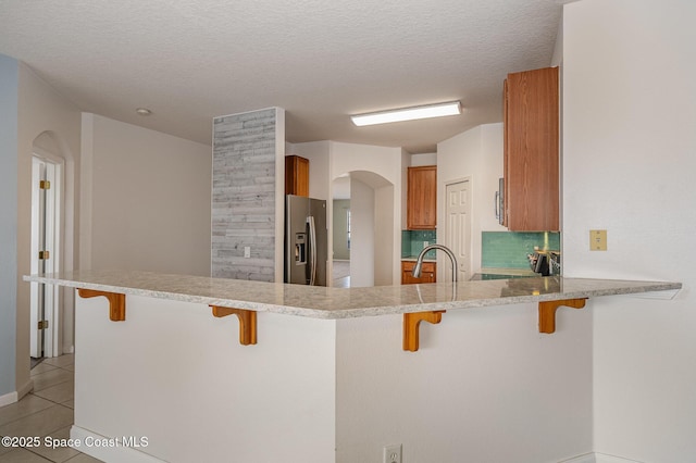 kitchen with light tile patterned floors, kitchen peninsula, appliances with stainless steel finishes, a textured ceiling, and a breakfast bar