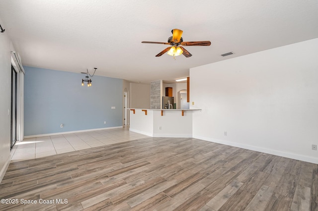 unfurnished living room featuring ceiling fan with notable chandelier and light hardwood / wood-style floors