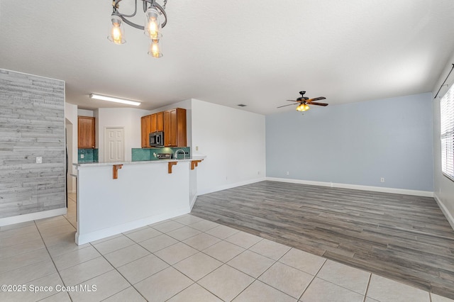 kitchen with a textured ceiling, pendant lighting, kitchen peninsula, light wood-type flooring, and a breakfast bar