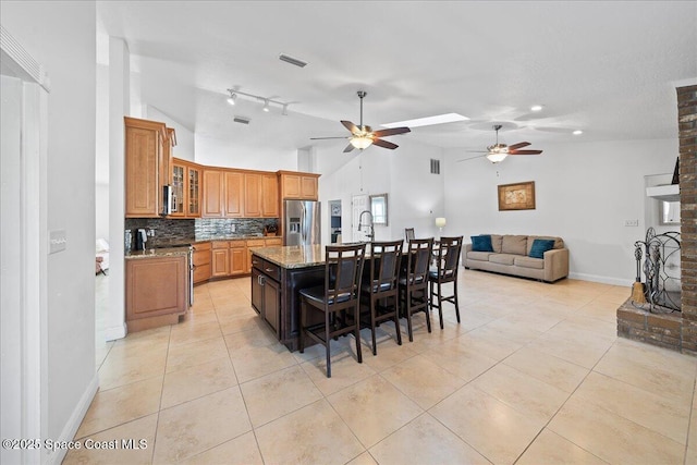 kitchen with appliances with stainless steel finishes, tasteful backsplash, a kitchen island with sink, light tile patterned floors, and light stone counters