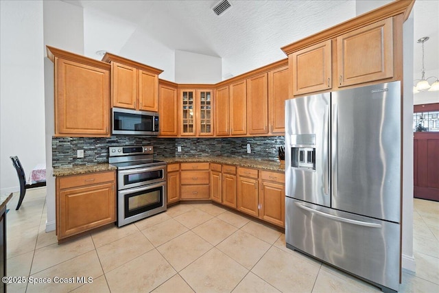 kitchen with appliances with stainless steel finishes, light tile patterned floors, decorative backsplash, and dark stone counters