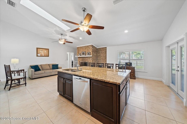 kitchen with sink, light stone counters, a center island with sink, dishwasher, and vaulted ceiling with skylight