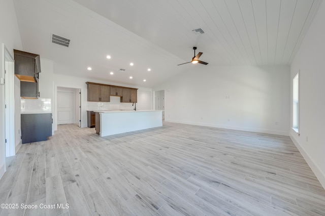 unfurnished living room with light wood-type flooring, ceiling fan, vaulted ceiling, and sink