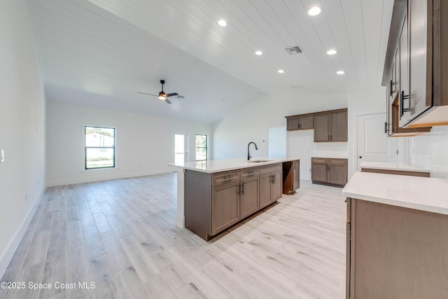 kitchen with an island with sink, ceiling fan, vaulted ceiling, light hardwood / wood-style flooring, and sink