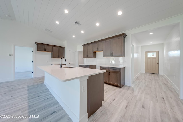 kitchen featuring light wood-type flooring, sink, vaulted ceiling, wooden ceiling, and a center island with sink