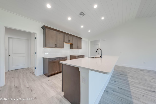 kitchen featuring light hardwood / wood-style floors, decorative backsplash, sink, a kitchen island with sink, and wooden ceiling