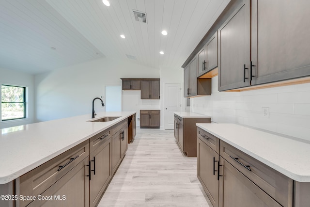 kitchen with lofted ceiling, wood ceiling, sink, a kitchen island with sink, and light hardwood / wood-style flooring