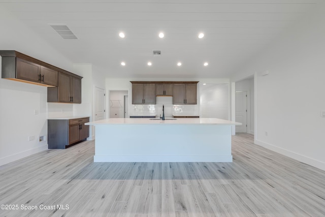 kitchen with light wood-type flooring, dark brown cabinetry, sink, and a center island with sink