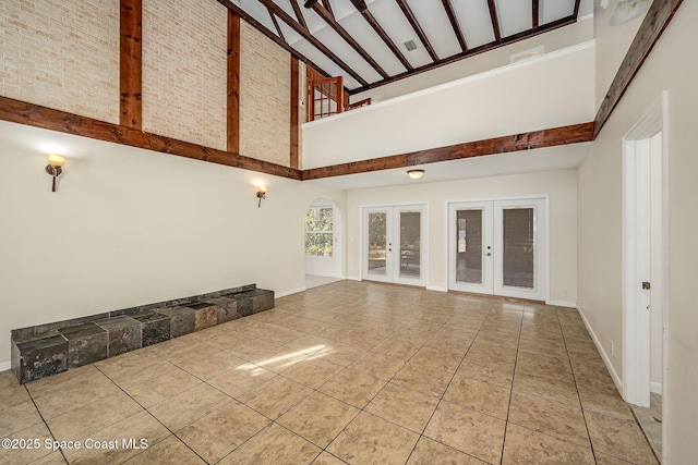 unfurnished living room with french doors, beam ceiling, high vaulted ceiling, and light tile patterned floors