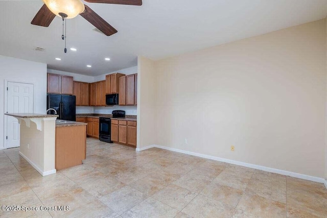 kitchen featuring black appliances, a kitchen island with sink, ceiling fan, a breakfast bar, and light stone counters