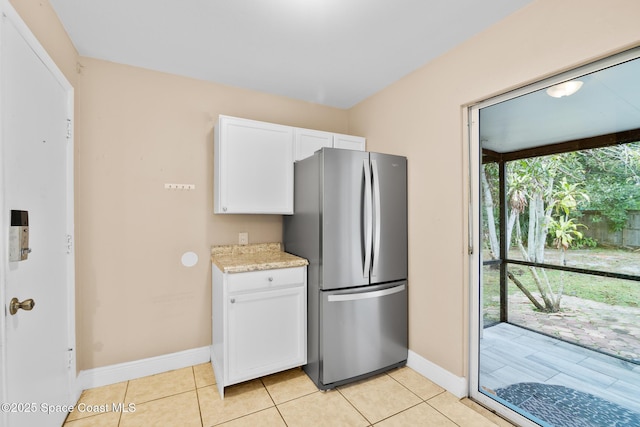 kitchen featuring light tile patterned flooring, white cabinetry, light stone countertops, and stainless steel refrigerator