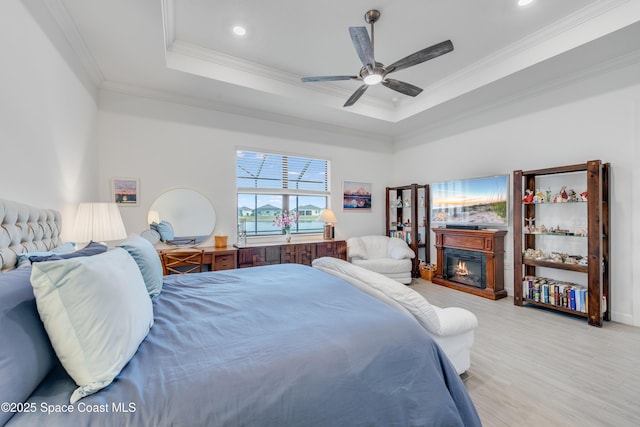 bedroom with ceiling fan, ornamental molding, light hardwood / wood-style floors, and a tray ceiling