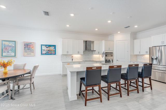 kitchen featuring white cabinets, a kitchen bar, wall chimney range hood, stainless steel appliances, and a center island with sink