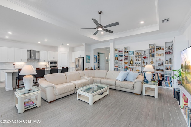 living room featuring a raised ceiling, ceiling fan, ornamental molding, and light hardwood / wood-style floors