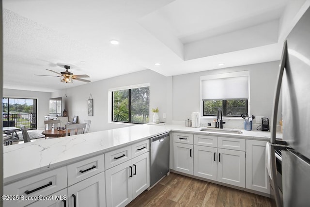 kitchen with appliances with stainless steel finishes, white cabinetry, sink, ceiling fan, and light stone counters