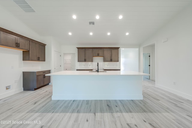 kitchen featuring light hardwood / wood-style floors, a kitchen island with sink, lofted ceiling, dark brown cabinets, and sink