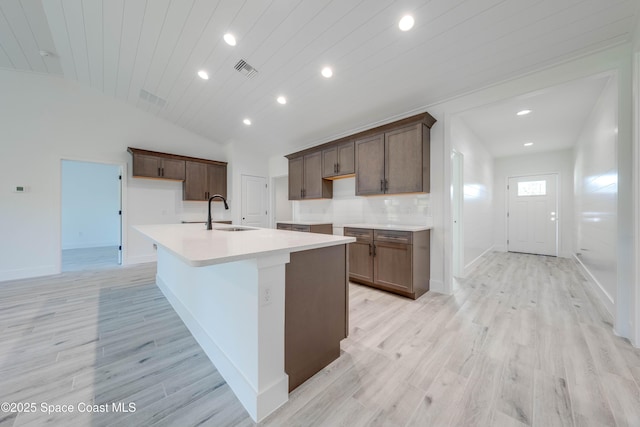 kitchen featuring sink, backsplash, light wood-type flooring, wooden ceiling, and a center island with sink