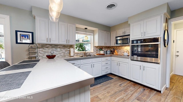 kitchen with appliances with stainless steel finishes, sink, white cabinets, hanging light fixtures, and kitchen peninsula