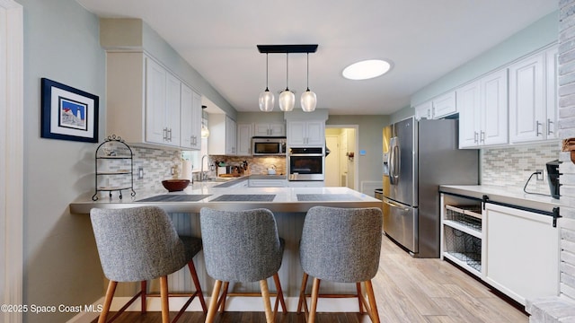 kitchen featuring appliances with stainless steel finishes, a breakfast bar area, white cabinets, hanging light fixtures, and kitchen peninsula