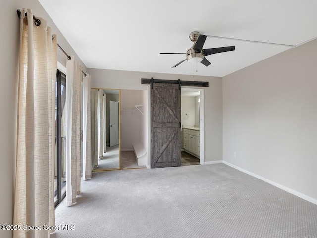 unfurnished bedroom featuring ceiling fan, carpet, a barn door, a spacious closet, and a closet