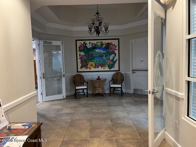 living area with french doors, ornamental molding, a tray ceiling, and a chandelier