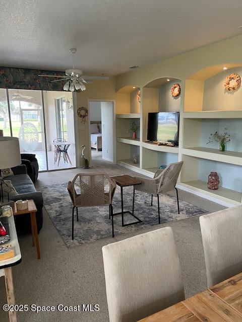 carpeted living room with ceiling fan, built in features, and a textured ceiling