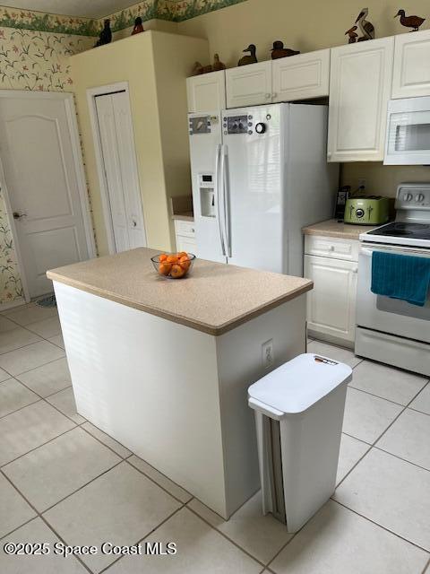 kitchen featuring white cabinetry, a kitchen island, light tile patterned flooring, and white appliances