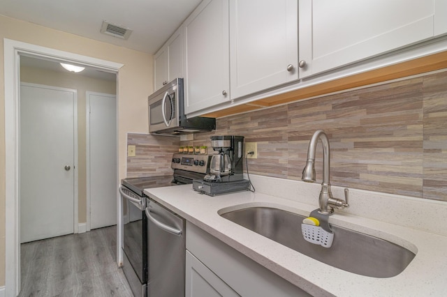 kitchen with white cabinetry, stainless steel appliances, tasteful backsplash, light wood-type flooring, and sink