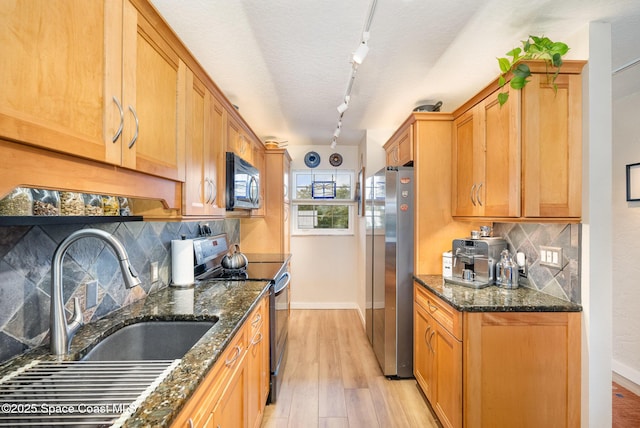 kitchen featuring backsplash, dark stone countertops, light hardwood / wood-style floors, sink, and stainless steel appliances