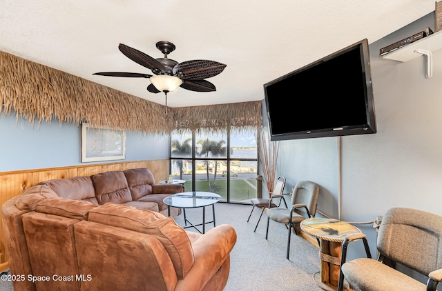 carpeted living room featuring ceiling fan and wood walls