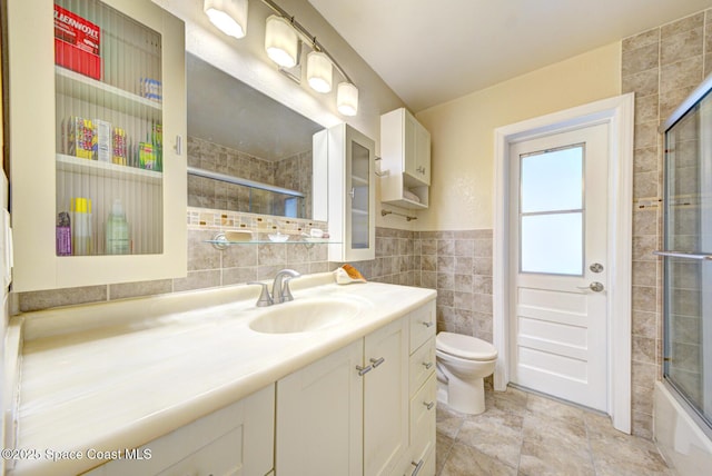 full bathroom featuring tile walls, vanity, enclosed tub / shower combo, and toilet