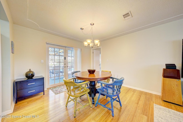 dining area featuring light hardwood / wood-style flooring, a notable chandelier, a textured ceiling, and french doors