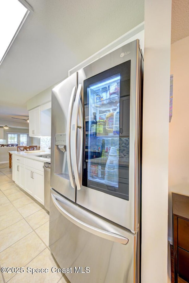 kitchen featuring light tile patterned flooring, tasteful backsplash, white cabinetry, stainless steel fridge, and a textured ceiling