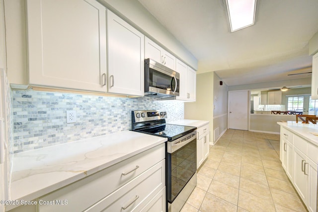 kitchen with light tile patterned floors, backsplash, stainless steel appliances, light stone countertops, and white cabinets