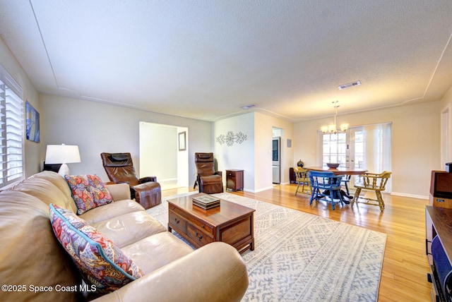 living room with an inviting chandelier, light wood-type flooring, a textured ceiling, and a wealth of natural light