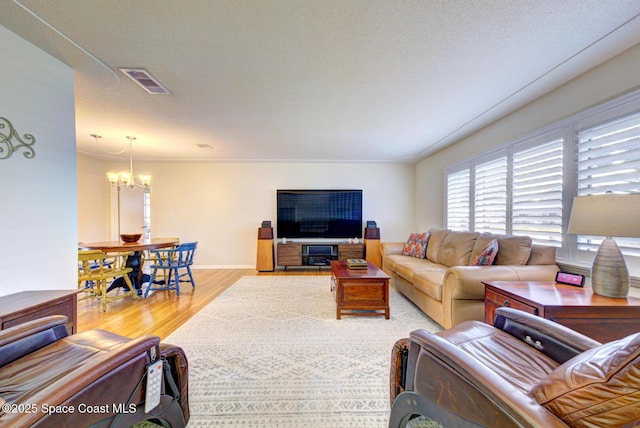 living room featuring hardwood / wood-style flooring, crown molding, a notable chandelier, and a textured ceiling