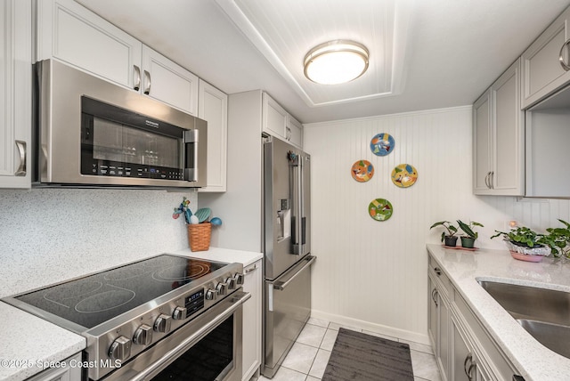 kitchen featuring stainless steel appliances, light stone countertops, sink, and light tile patterned floors