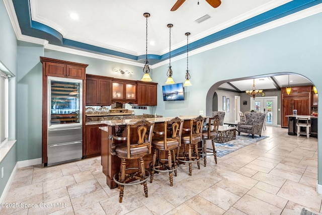 kitchen featuring stainless steel built in refrigerator, a breakfast bar area, ceiling fan with notable chandelier, and hanging light fixtures