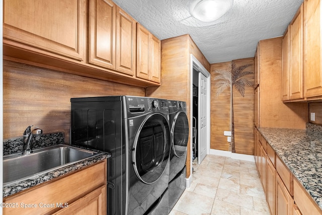 laundry area featuring washer and dryer, wood walls, sink, cabinets, and a textured ceiling