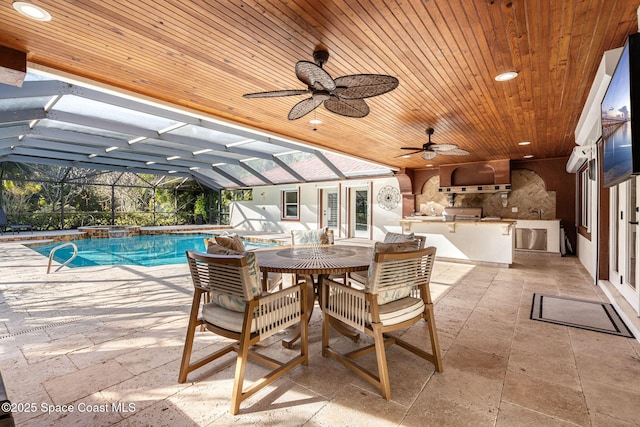 view of pool with ceiling fan, a patio, glass enclosure, a grill, and an outdoor kitchen