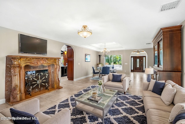 tiled living room featuring a notable chandelier, a tray ceiling, and a high end fireplace