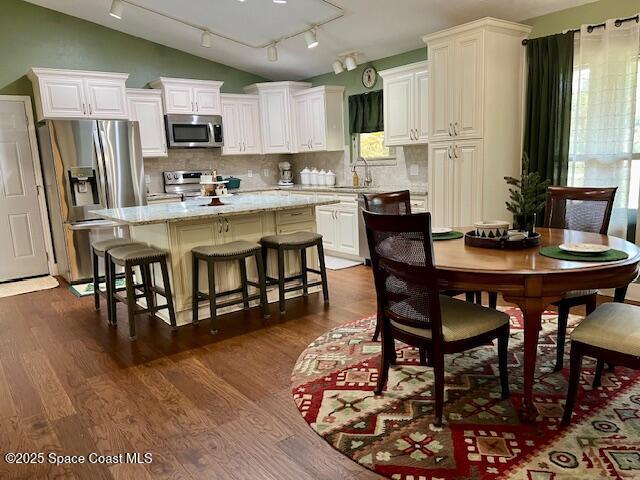 kitchen featuring white cabinetry, appliances with stainless steel finishes, tasteful backsplash, lofted ceiling, and a center island