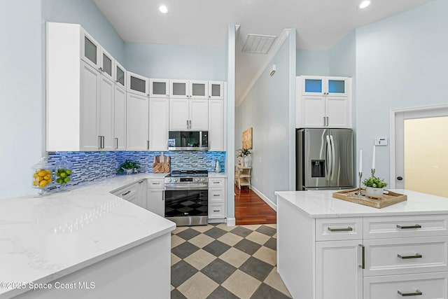 kitchen with tasteful backsplash, light stone countertops, light floors, white cabinets, and stainless steel appliances