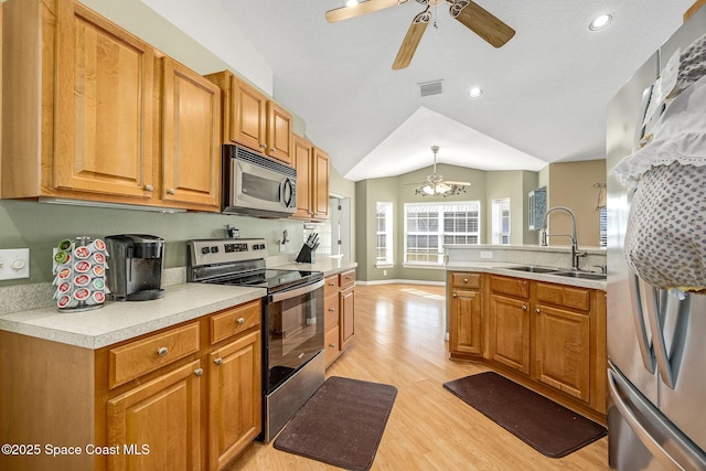 kitchen featuring stainless steel appliances, decorative light fixtures, light wood-type flooring, lofted ceiling, and sink