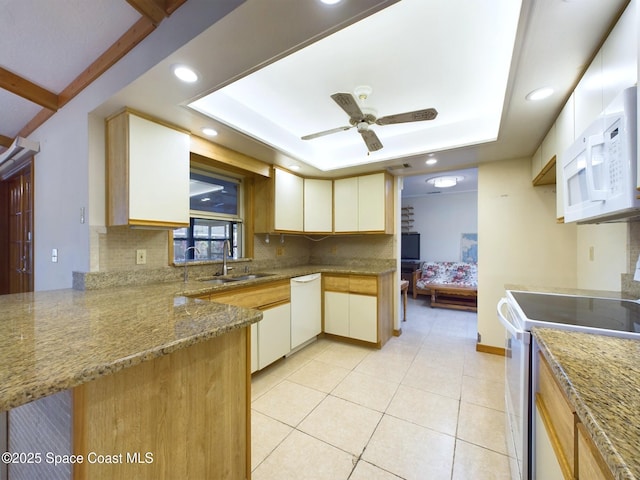 kitchen featuring light tile patterned floors, a tray ceiling, kitchen peninsula, white appliances, and backsplash